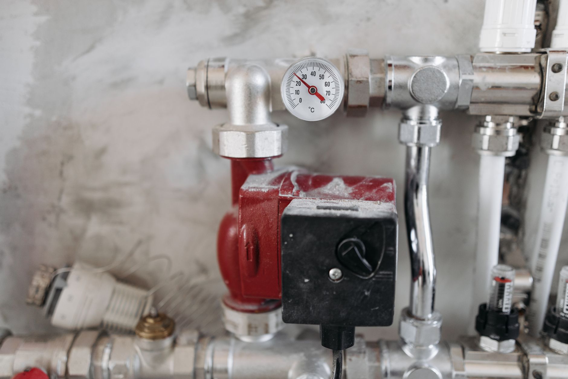 Circulateur rouge et thermomètre à aiguille sur une nourrice de tuyaux chromés d'un circuit de chauffage
