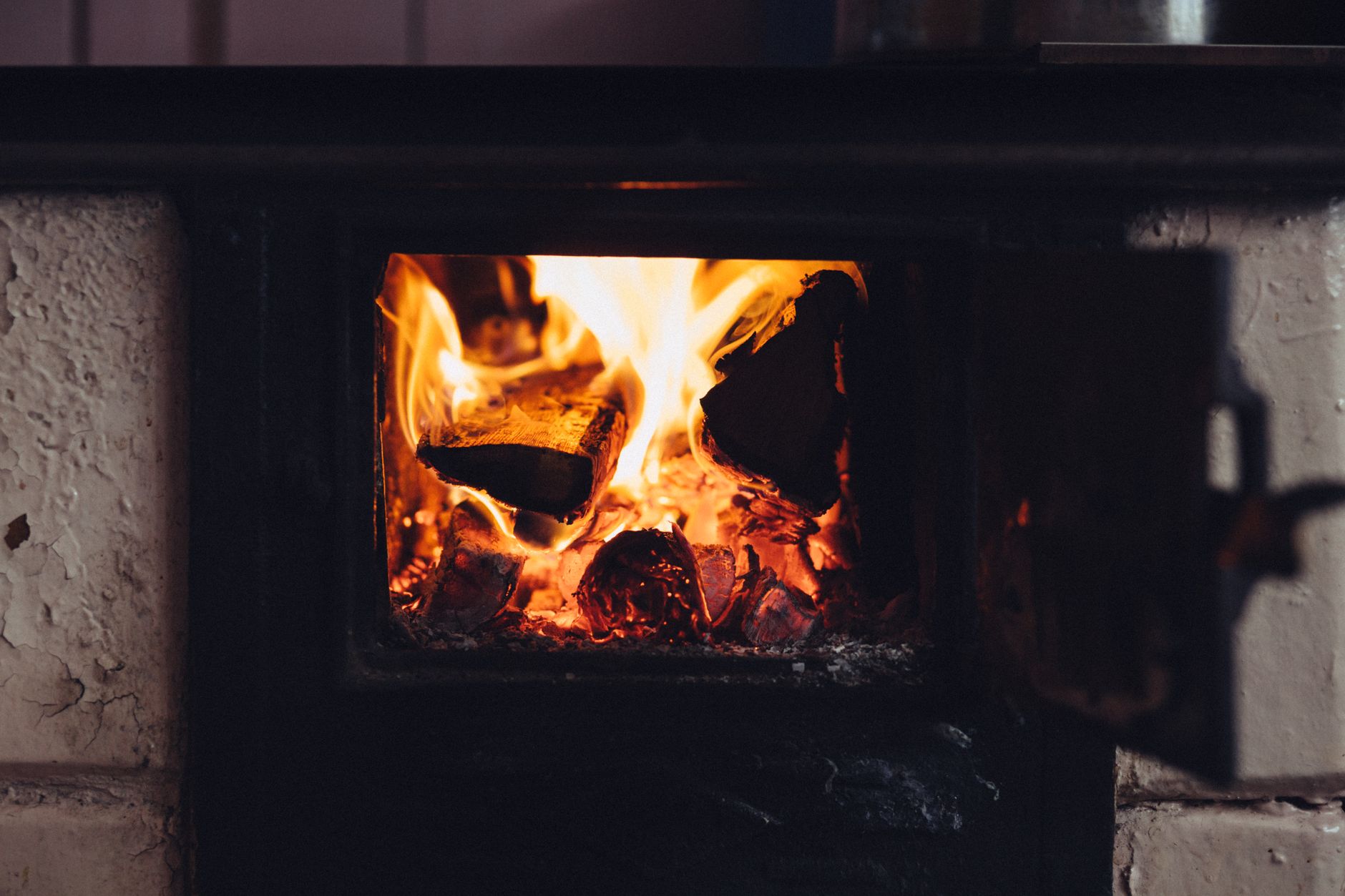 Un poêle à bois allumé dans un salon, avec de la fumée visible à l'extérieur par la fenêtre