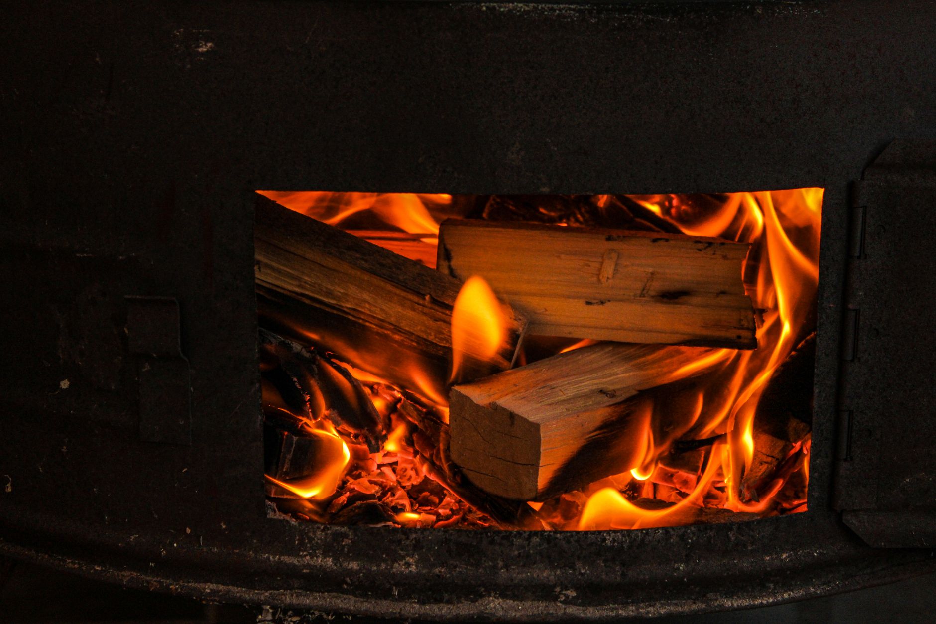 Bûches qui flambent derrière l'ouverture d'un poêle à bois en fonte noire, vues de près