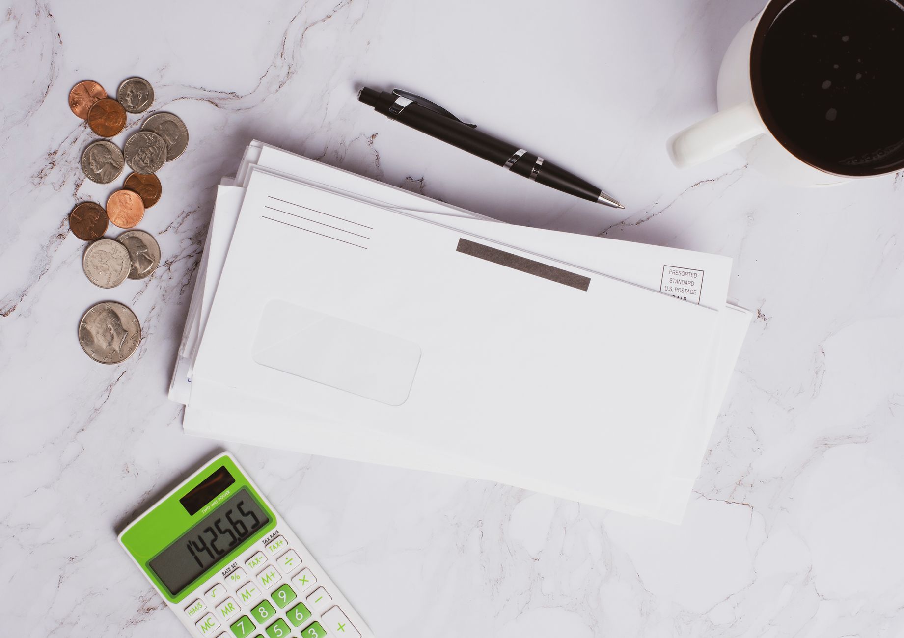 Documents financiers, calculatrice, pièces de monnaie et tasse de café posés à plat sur une surface en marbre