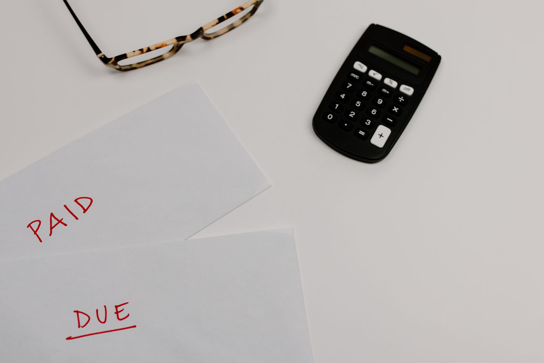Vue de dessus de documents financiers marqués « Paid » et « Due » posés près d'une calculatrice et de lunettes