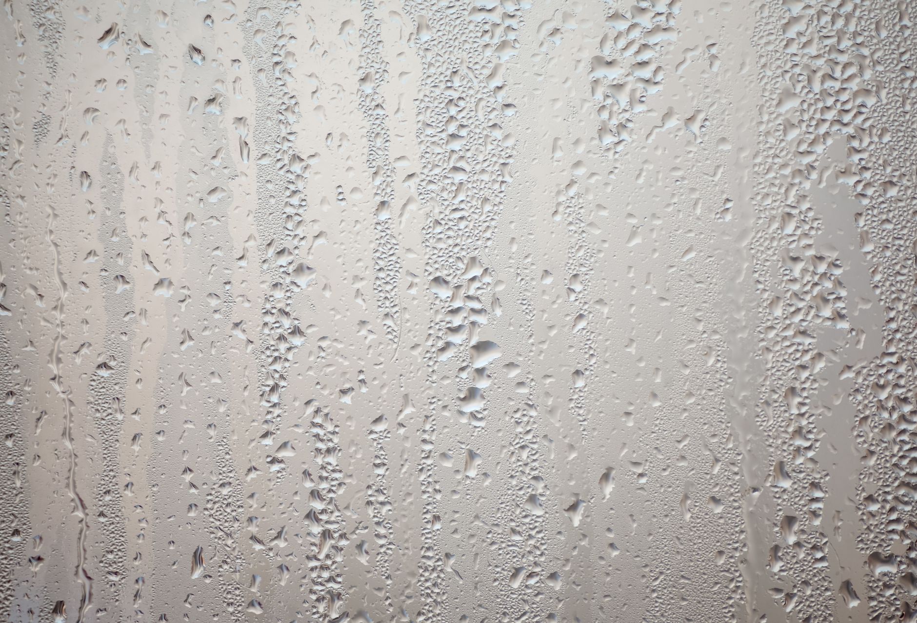 Gouttes de condensation ruisselant sur une vitre embuée en formant de longues traînées verticales