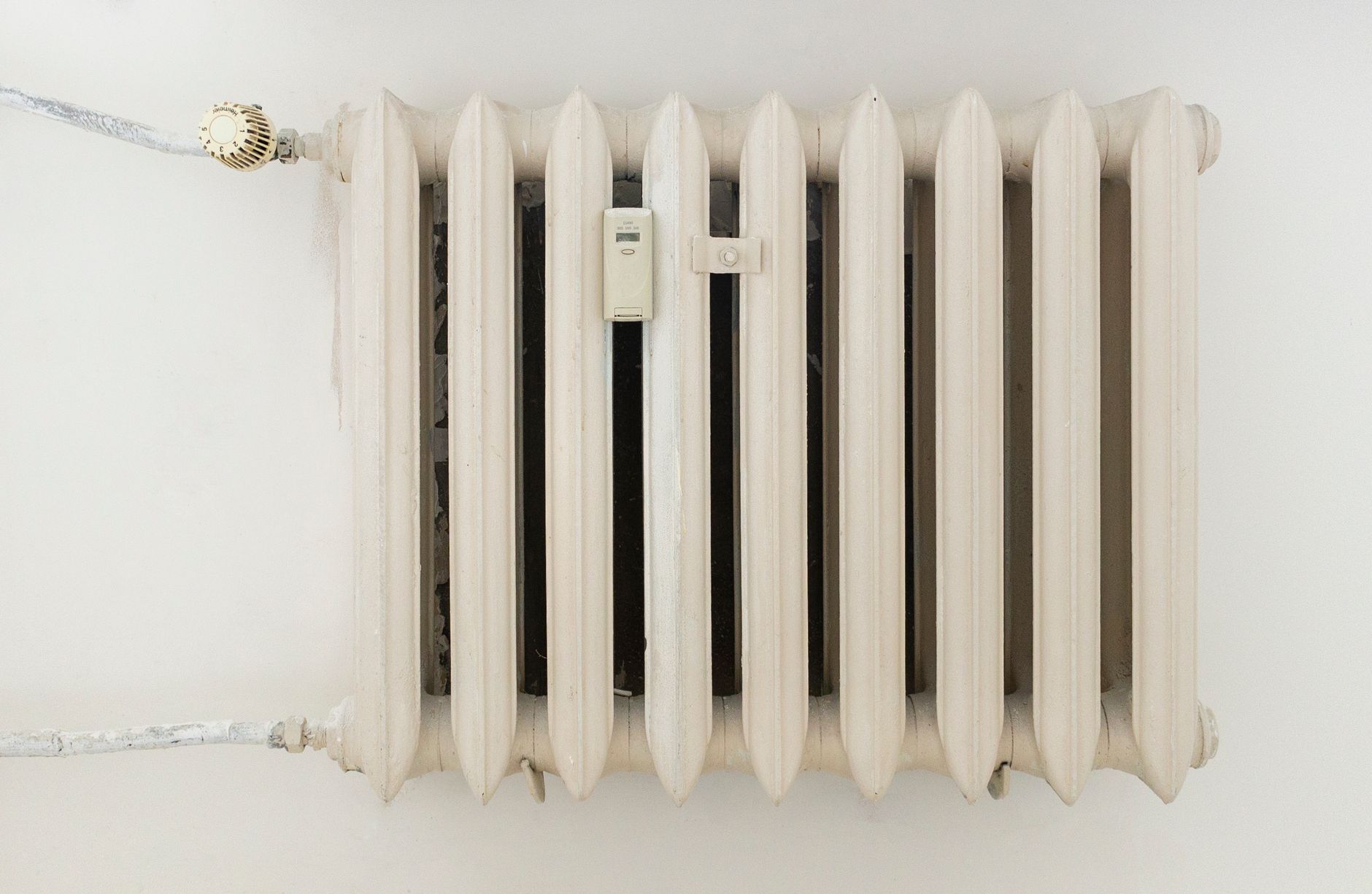 Main réglant le robinet thermostatique d'un radiateur près d'une fenêtre ensoleillée au printemps