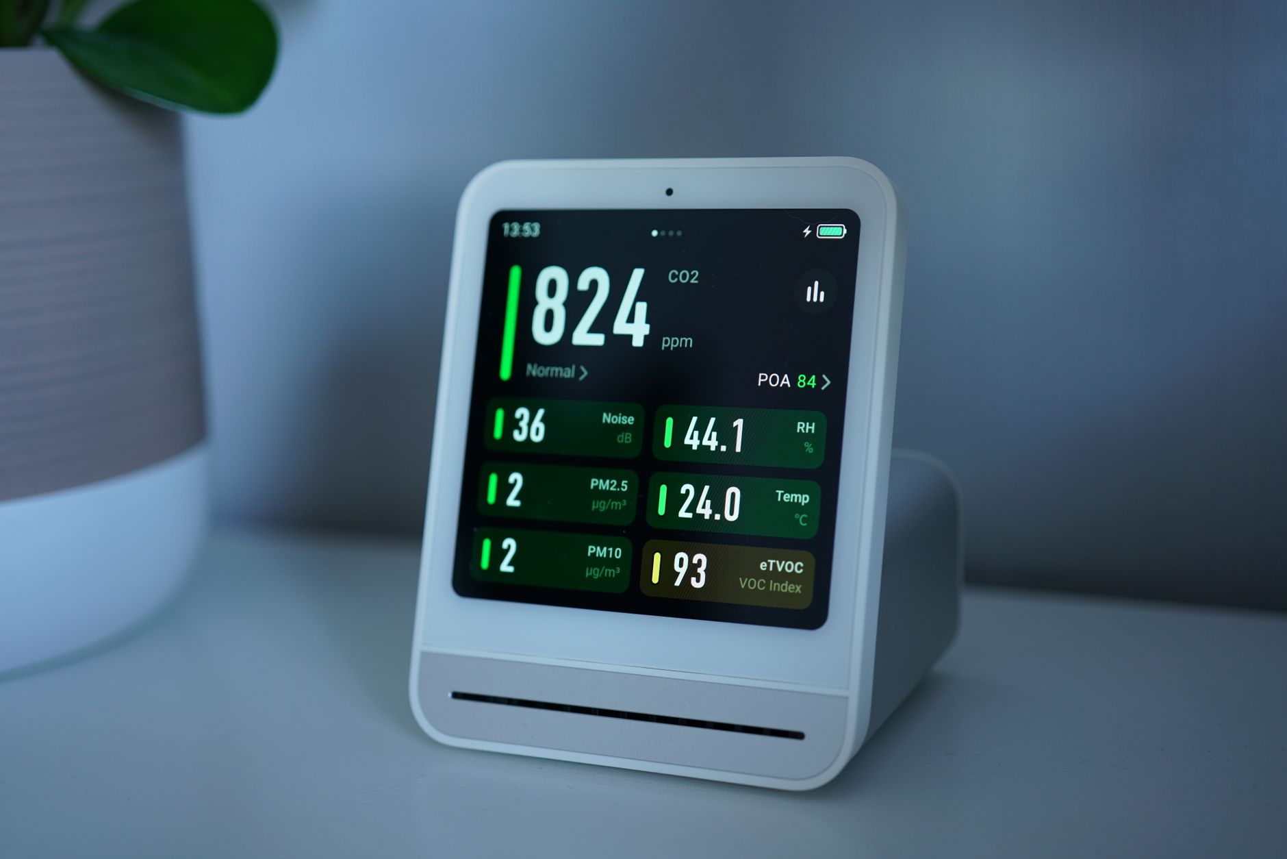 Moniteur de qualité de l'air affichant un taux de CO2 de 824 ppm, posé sur un meuble près d'une plante verte