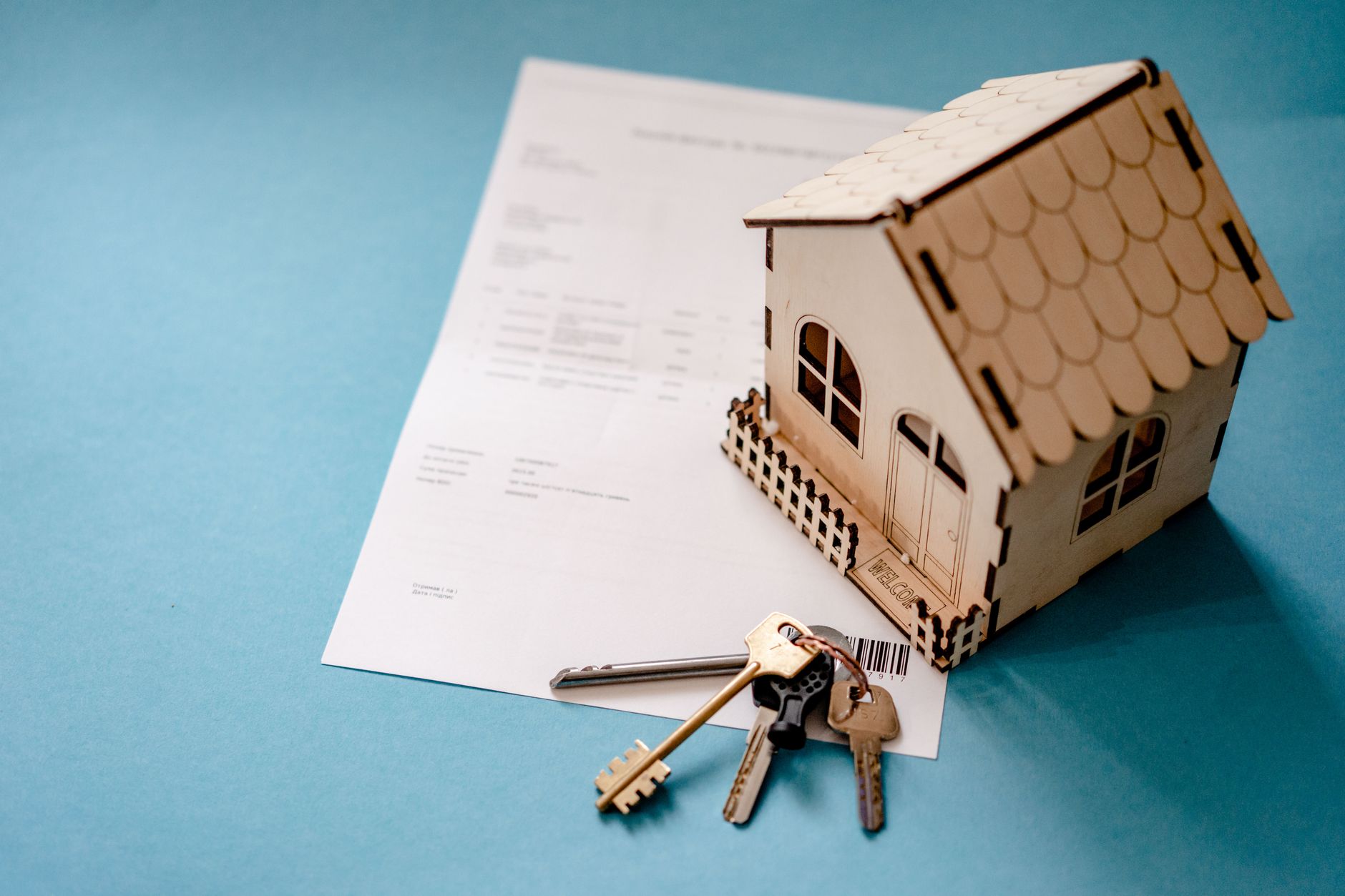 Maquette de maison en bois posée sur un contrat imprimé, à côté d'un trousseau de clés, sur fond bleu