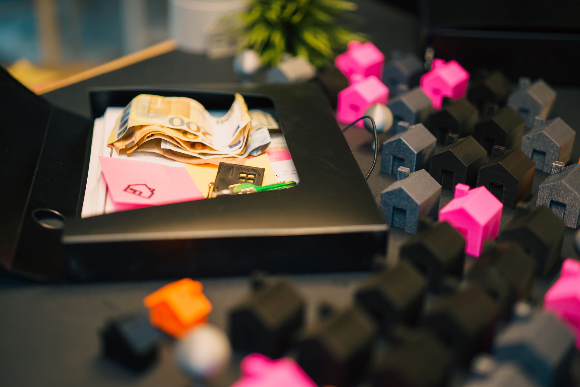 Billets en euros et clé rangés dans un classeur noir, entourés de petites maisons miniatures colorées
