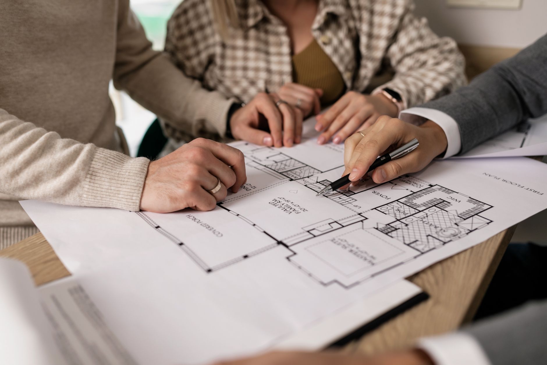 Un conseiller en rénovation énergétique explique un projet de travaux à un propriétaire, plans et documents sur la table