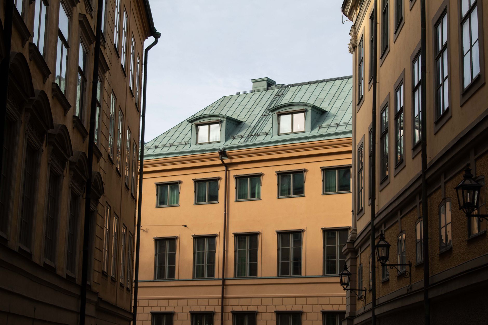 Façades d'immeubles anciens aux tons ocre et toit vert à lucarnes, vues depuis une ruelle étroite