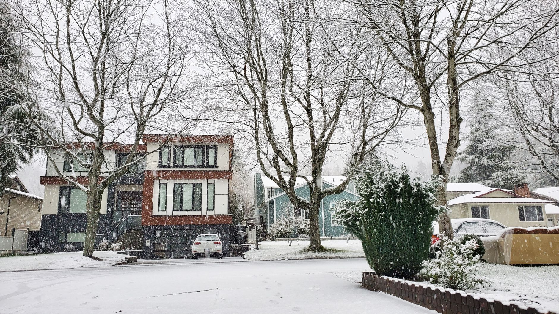 Maisons modernes d'un quartier résidentiel sous une chute de neige, arbres nus et voiture garée devant