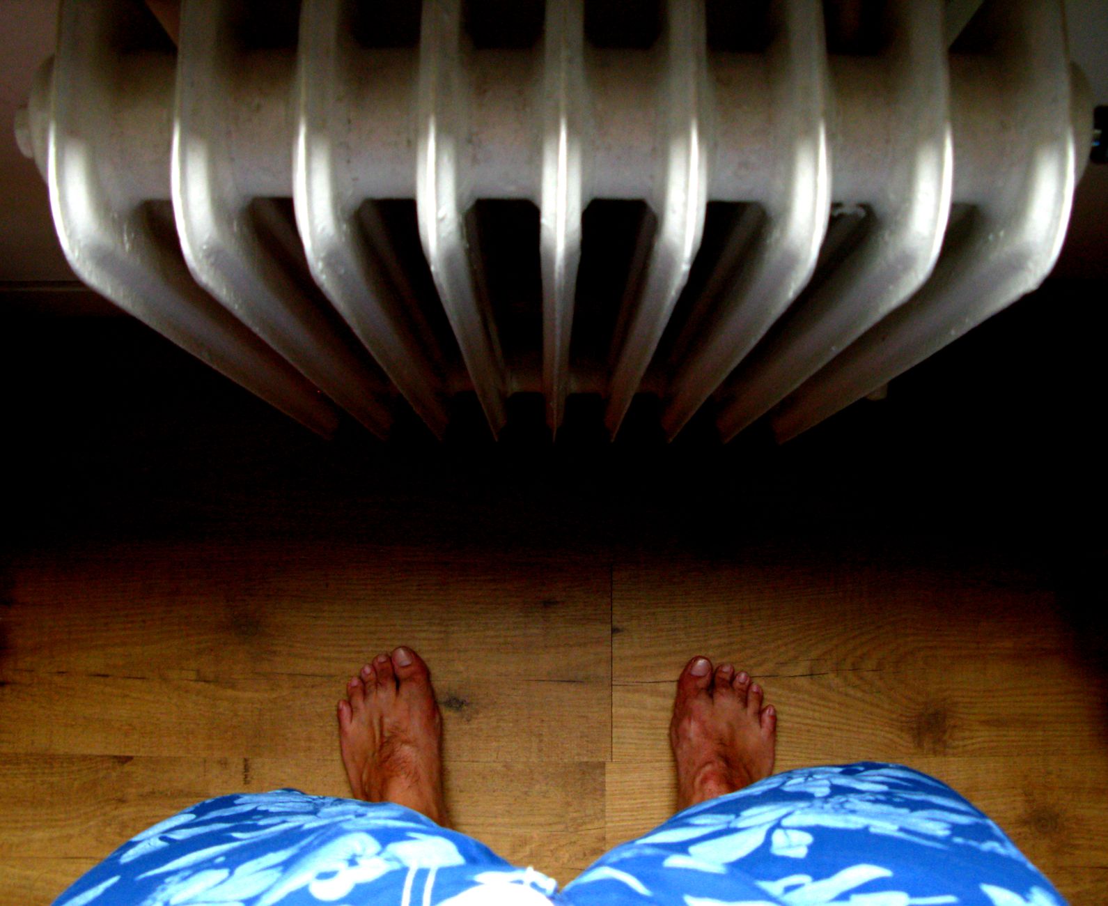 Vue plongeante de pieds nus posés sur un parquet en bois à proximité d'un radiateur dans un logement