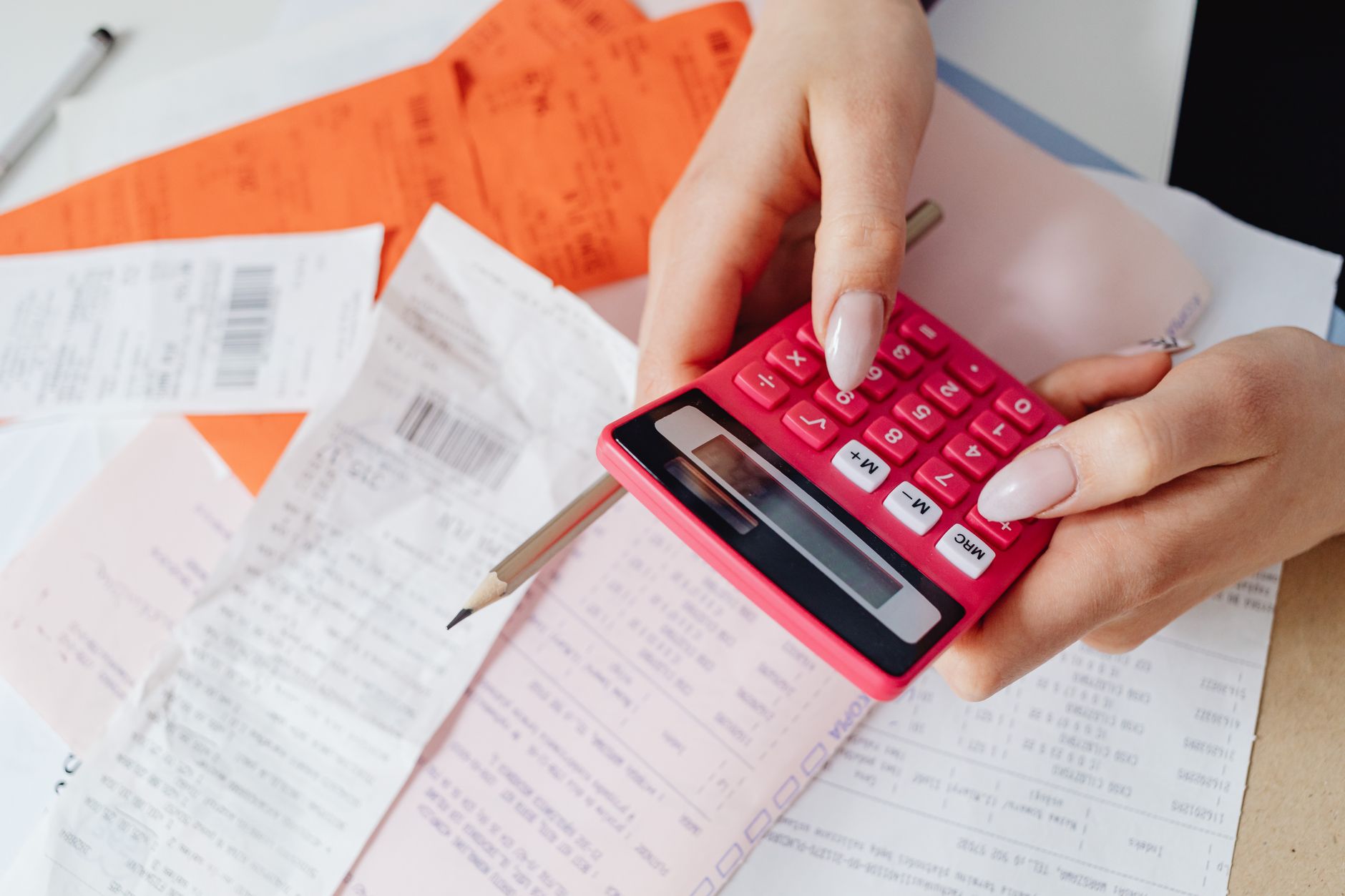 Mains tapant sur une calculatrice rose au-dessus de tickets de caisse et de factures étalées sur une table