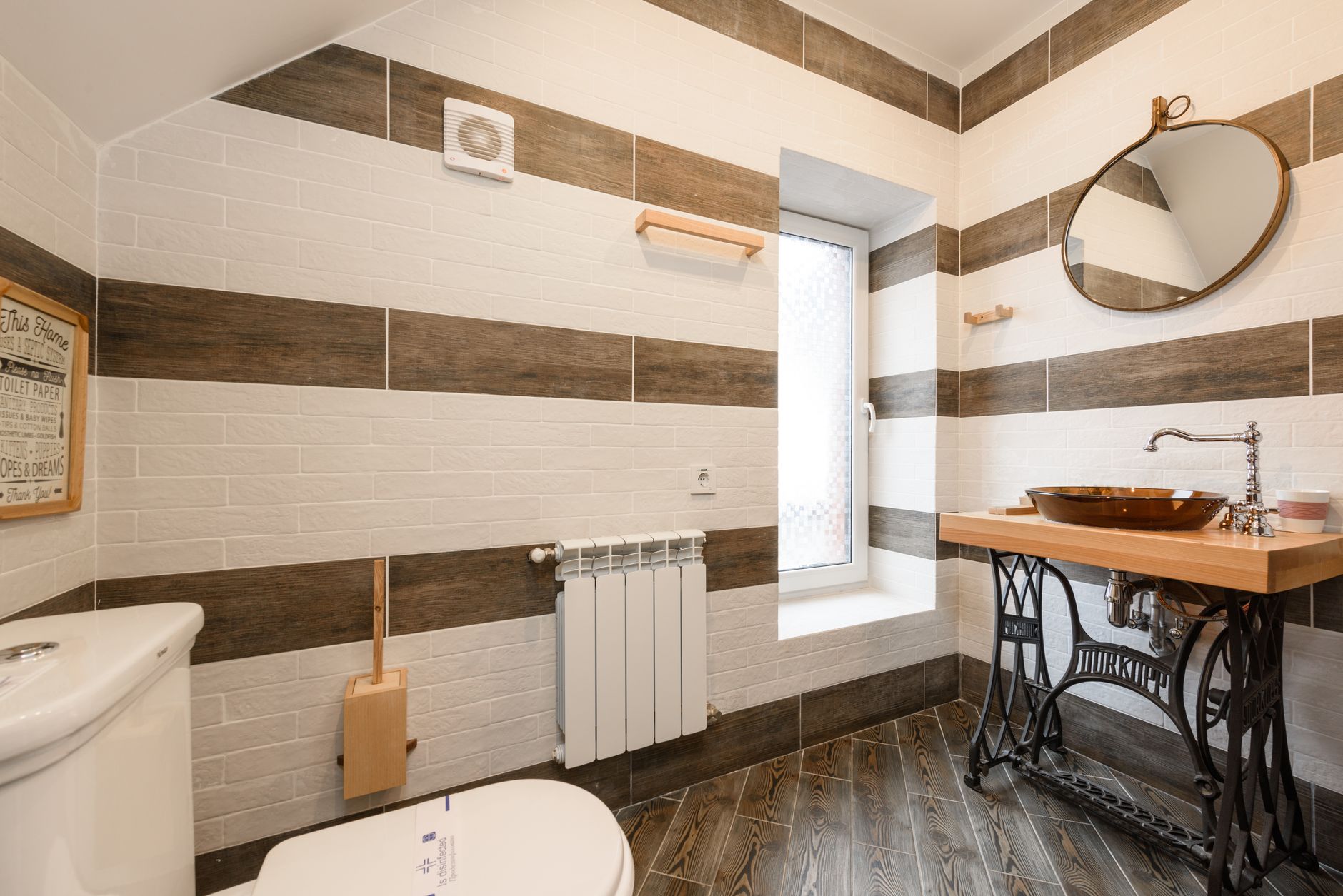 Salle de bains carrelée avec un aérateur d'extraction carré fixé en haut du mur, au-dessus d'un radiateur blanc